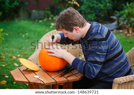 Young man making jack-o-lantern for halloween in autumn garden
