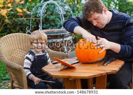 Young father and his little son making jack-o-lantern pumpkin for halloween in autumn garden