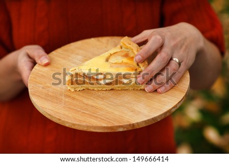 Fresh baked apple pie on wooden cutting board holding by hand of a woman