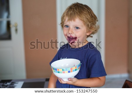 Little toddler boy with dirty face eating fresh blueberry indoor