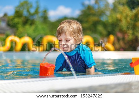 Cheerful toddler playing with water by the outdoor swimming pool