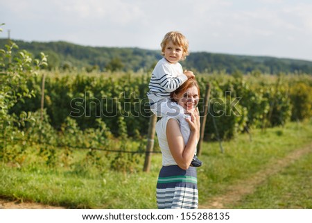 Young mother giving little boy a ride on shoulders on countryside in Germany
