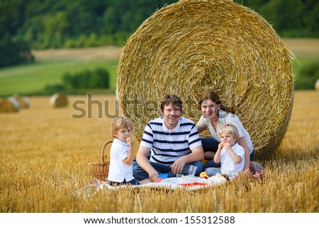 happy family of four picnicking on yellow hay field in summer