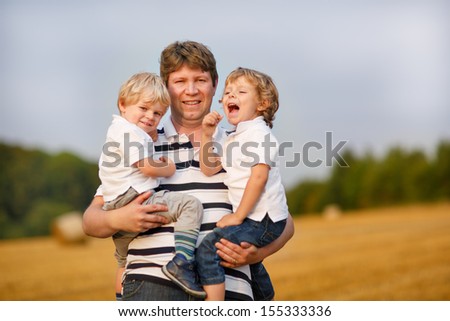 Young man and two little sons having fun on yellow hay field in summer