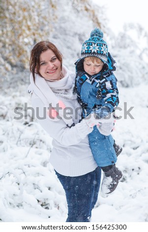 Young woman and her little son having fun with snow in winter forest