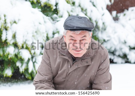 Portrait of senior man with snow outdoors on beautiful winter day