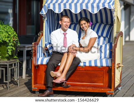 Beautiful indian bride and caucasian groom, in beach chair