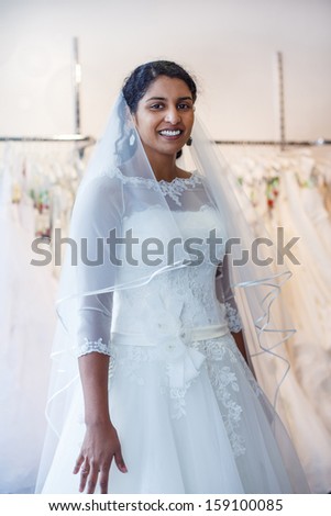 Young indian woman in wedding dress with bridal gowns on display in boutique.