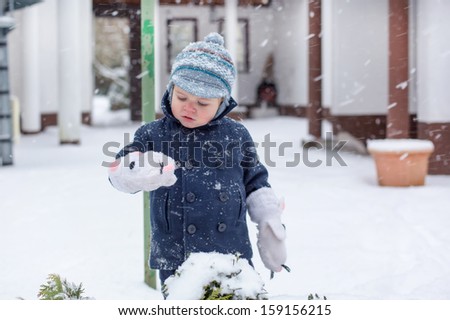 Cute baby boy in winter clothes playing with snow