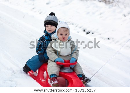 Two little siblings having fun on sledge on winter snow day