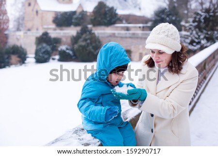 Young mother and little toddler boy having fun with snow outdoors.