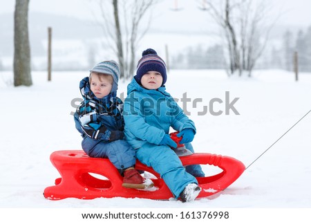 Two little siblings having fun on sledge on winter snow day in mountains