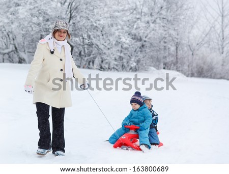 Two little siblings and their mother having fun on sledge on winter day in mountains