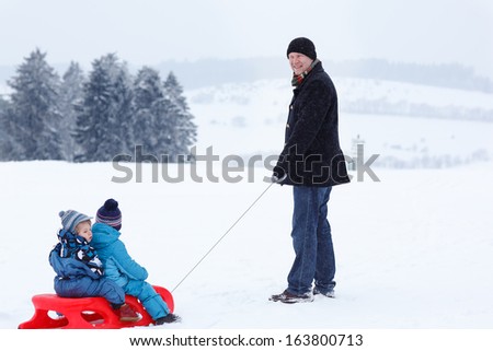 Two little siblings and their father having fun on sledge on winter snow day