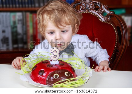 Cute three year old boy celebrating his birthday and blowing off the candles on the cake