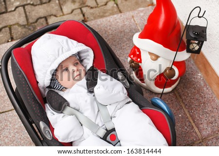 Little baby toddler in white winter clothes sitting in car seat