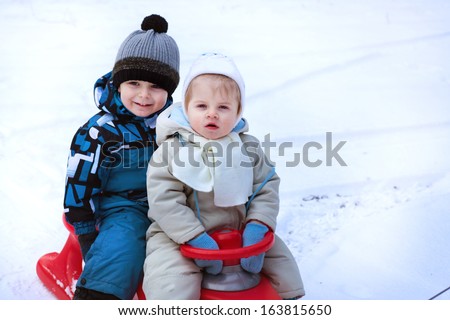 Two little siblings having fun on sledge on winter snow day