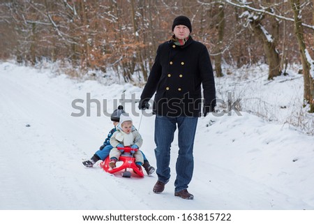 Two little siblings and their father having fun on sledge on winter snow day