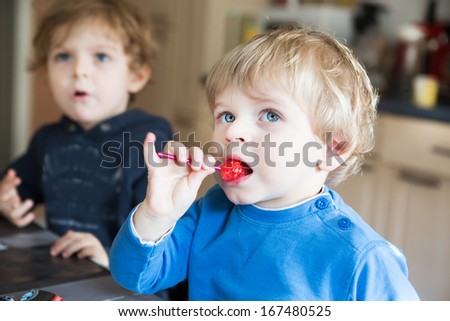 Two little siblings boys watching tv and eating candy indoor. Selective focus on one boy.