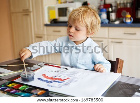 Adorable happy boy of two years drawing with paints