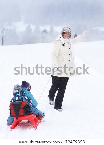 Two little siblings and their mother having fun on sledge on winter day in mountains