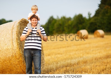 Happy family of two: Young father and his little son having fun on yellow hay field in summer