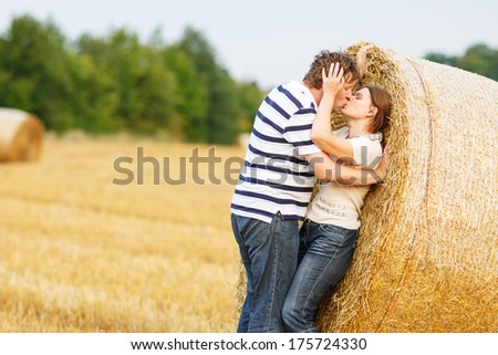 Happy young couple in love on yellow hay field on summer evening, kissing and hugging