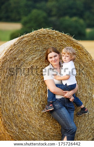 Young mother and her little son having fun on yellow hay field in summer