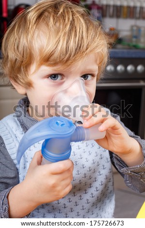 Adorable toddler boy making inhalation with nebulizer and inhalator in home kitchen