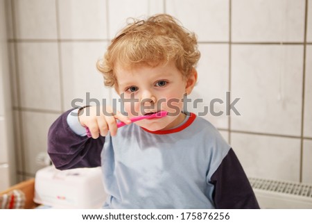 Adorable toddler with blue eyes and blond hair brushing his teeth