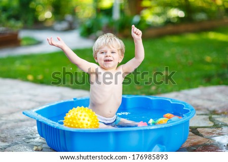 Little toddler boy having fun with splashing water and playing ball in summer garden pool