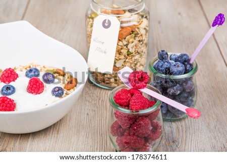 Fresh yoghurt with home made cereals and muesli, fresh raspberry and blueberry on wooden textured background as healthy breakfast