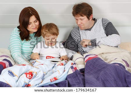 Happy family: Mother, father and little son reading book before going to bed
