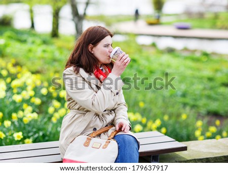 Young woman drinking coffee in spring park