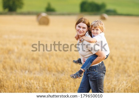 Happy family of two: Young mother and little toddler boy walking on yellow hay field in summer