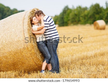 Happy young couple in love on yellow hay field on summer evening, kissing and hugging