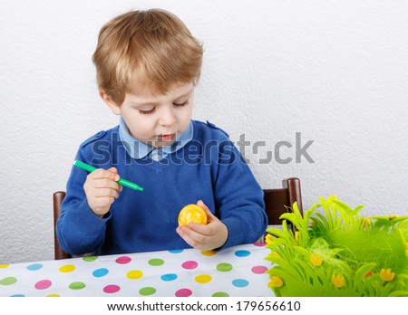 Little toddler boy painting colorful Easter egg for hunt, traditional action in Germany for Eastern holiday