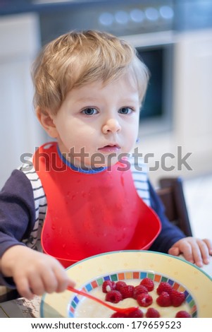 Portrait of cute toddler boy eating sitting in home kitchen and eating milk mash with berry