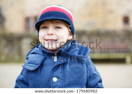 Portrait of adorable caucasian toddler boy in warm clothes having fun on cold day, outdoors