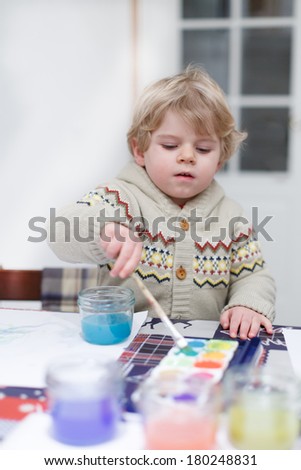 Cute toddler boy having fun indoor, painting with different paints colors