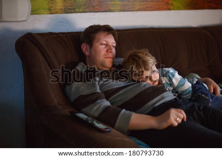 Cute little boy and his father watching tv, indoors in dark room at the evening