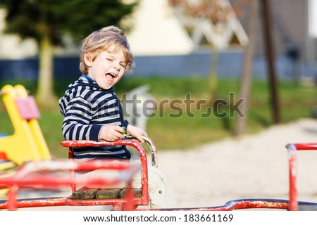 Little toddler boy having fun on old carousel on outdoor playground.