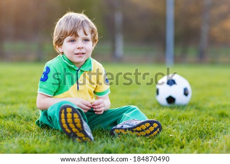 Funny little boy of 4 having fun with playing soccer with football on football field, outdoors.