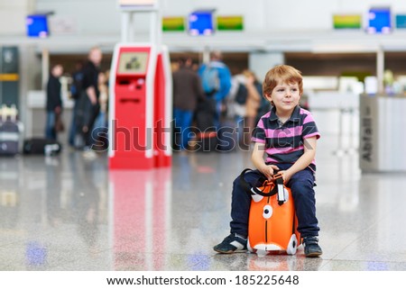 Beautiful blond boy having fun wiht suitcase at airport, indoors. Going on holidays.