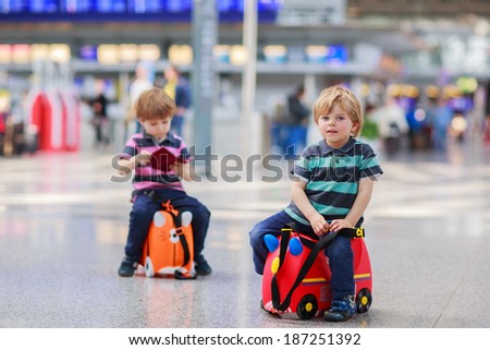 Two little sibling boys having fun and going on vacations trip with suitcase at airport, indoors.