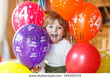 Happy little boy celebrating his 4 birthday with colorful balloons, indoor in kids room.