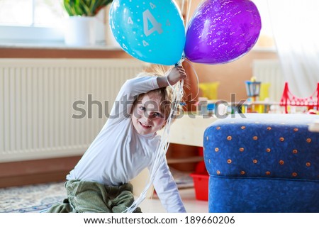 Happy little boy celebrating his 4 birthday with colorful balloons, indoor in kids room.
