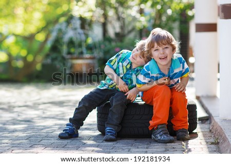 Two little sibling boys hugging and having fun outdoors, in home\'s garden.