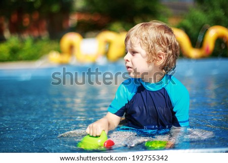 Cute boy of 3 years in protection swimming suit having fun with water in outdoor swimming pool