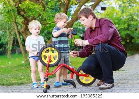 Happy family of three person: Two little sibling  boys repairing broken bicycle wheel with father in summer, outdoors